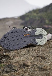 Trailrunning-Schuhsohle mit tiefem Profil und Continental-Logo, liegend auf felsigem Untergrund im Freien mit unscharfem natürlichem Hintergrund.