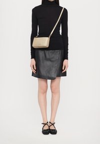 Sort langærmet turtleneck, læder A-line nederdel, guld crossbody taske og sorte sko med krydsede stropper og nitter.