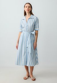 Abito a righe blu e bianche con colletto, maniche corte, bottoni sul davanti e vita legata. Tessuto leggero con un design fluido.
