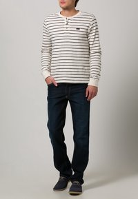 Rutigt långärmat skjorta i kräm och marinblått, med knappstängning vid halsen. Kombinerad med mörkblåjeans och mörka skor.