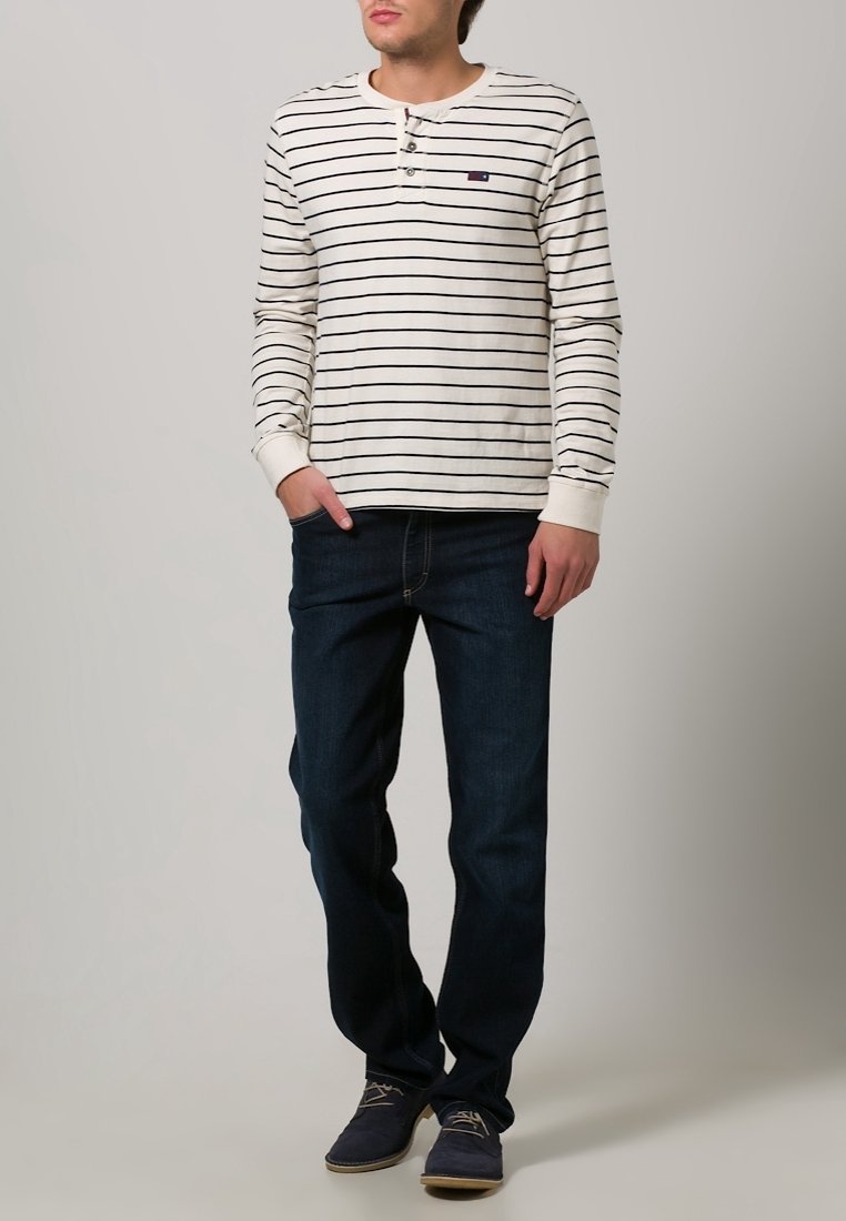 Rutigt långärmat skjorta i kräm och marinblått, med knappstängning vid halsen. Kombinerad med mörkblåjeans och mörka skor.