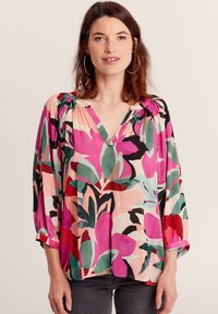 Blusa floreale con scollatura a V, maniche a tre quarti e motivi di foglie rosa brillante, rosse e verdi su uno sfondo chiaro. Tessuto morbido.