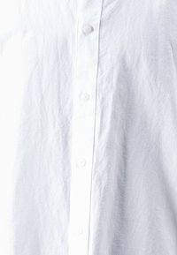 Camicia bianca button-up realizzata in tessuto stropicciato. Presenta una linea di bottoni verticale, una texture morbida e un design del colletto standard.