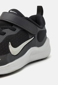 Baskets noires avec une tige en mesh, des accents synthétiques et un logo swoosh réfléchissant en argent. Semelle intermédiaire blanche épaisse avec une surface texturée.