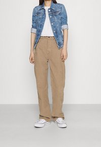 Ljusblå jeansjacka över en vit T-shirt, tillsammans med beige corduroy byxor med vida ben och vita sneakers, med en avslappnad passform.