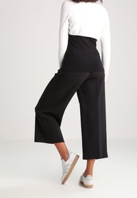 Czarne spodnie o szerokich nogawkach w połączeniu z białym, długim rękawem; posiadają dopasowany gorset i luźny krój. Teksturowany dzianinowy materiał i gładka tkanina.