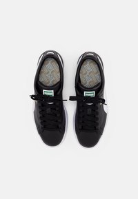 Scarpe sportive nere con tomaia in pelle liscia, lacci neri piatti e soletta grigia testurizzata con motivi geometrici.