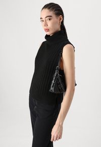 Svart ärmlös tröja med hög krage, med ribbat mönster. Bärs med svarta jeans och en liten svart handväska med kedjedetaljer.