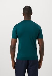 Short-sleeve teal athletic shirt made from smooth fabric, featuring a fitted design and subtle shoulder accents.