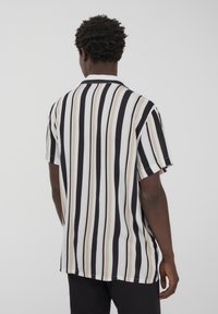 Camicia a maniche corte con righe verticali nere, bianche e beige, colletto classico e vestibilità ampia. Tessuto dalla superficie liscia.