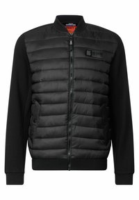 Svart jacka med vadderad framsida och ribbade ärmar. Har dragkedjeslutning, sidofickor och en märkt lapp på bröstet.