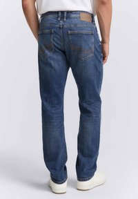 Jeans in denim blu scuro con taglio dritto, caratterizzati da due tasche posteriori, dettagli di cucitura discreti e un'etichetta in pelle marrone in vita.