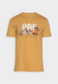 T-shirt jaune à manches courtes présentant un design graphique de montagnes et d'arbres avec "GAP" en lettres blanches en gras sur le devant.