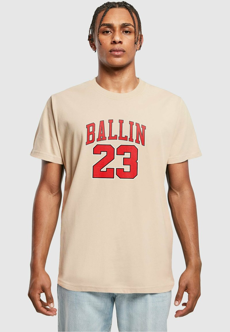 Smėlio spalvos medvilnės marškinėliai su raudonu užrašu "BALLIN" virš skaičiaus "23." Trumpi rankoviai ir laisvas fasonas.
