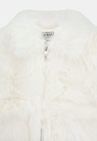 Giacca in pelliccia sintetica bianca con una texture morbida, colletto e chiusura con zip. L'etichetta interna riporta il nome del marchio "GUESS."