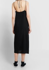 Robe midi noire sans manches avec un dos ouvert, fines bretelles et fentes sur les côtés, associée à des baskets montantes noires. Tissu léger.