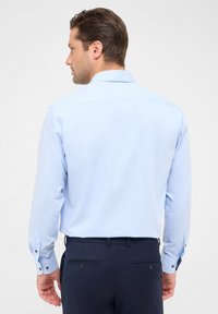Lichtblauw overhemd met lange mouwen en een standaard kraag, met knoopmanschetten en een gladde stof, gecombineerd met donkere broek met achterzakken.