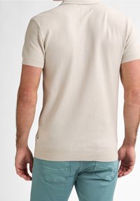 Beige kortärmad polo med en strukturerad mönster, ribbad krage och ärmslut. Bärs med ljusblå, något slitna chinos.