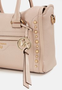 Borsa a tracolla in pelle rosa chiaro con accenti dorati, borchie decorative sui lati e un charm con logo appeso. Presenta doppi manici per il trasporto.