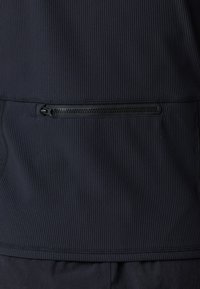 Marinblå zip-jacka med ribbad textur, med en horisontell dragkedjeficka på baksidan och platta sömmar vid nederkanten och sidorna.