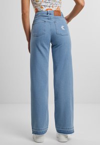 Svetlomodré vysoké široké džínsy vyrobené z denimu, s dvoma zadnými vreckami s logom a rozstrapkaným lemom na členkoch.