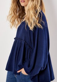 Dunkelblauer, strukturierter Pullover mit ausgestellter Silhouette und Rüschendetail am Bund. Verfügt über weite Ärmel und ein lässiges Design.