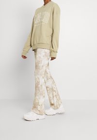 Sudadera verde claro de gran tamaño con logo blanco, combinada con pantalones de campana en tonos crema y beige con efecto tie-dye y zapatillas blancas gruesas.