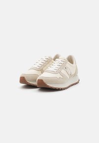 Beige athletic shoes with a suede and fabric upper, white laces, a rubber sole, and wavy accents along the sides.