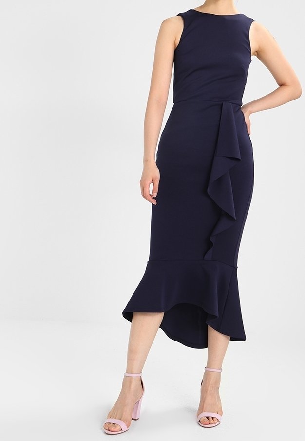 Robe midi sans manches bleu marine avec volants asymétriques sur le devant et à l'ourlet, associée à des sandales à talons blocs à bride cheville rose clair.