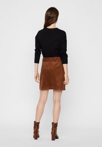 Een bruine corduroy rok gecombineerd met een zwarte longsleeve top en bruine haklaarzen, met een eenvoudig ontwerp en een hoog uitgesneden pasvorm.