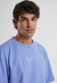 Light blue cotton t-shirt featuring short sleeves and a round neckline, with a white signature design on the front.