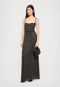 Black, floor-length dress with vertical striped pattern, thin straps, fitted bodice, and textured fabric. Matched with a black handbag.