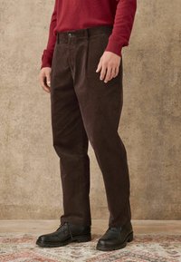 Braune Cordhosen mit geradem Schnitt, ausgestattet mit einem oberen Knopf, Taschen und einem strukturierten Stoff, kombiniert mit schwarzen Schnürstiefeln.