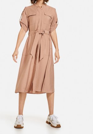 Helles rosa, kurzärmliges Kleid mit einem Knopfkragen, zwei Brusttaschen, Taillenbindeband und midi-langer Passform, kombiniert mit klobigen weißen Sneakers.