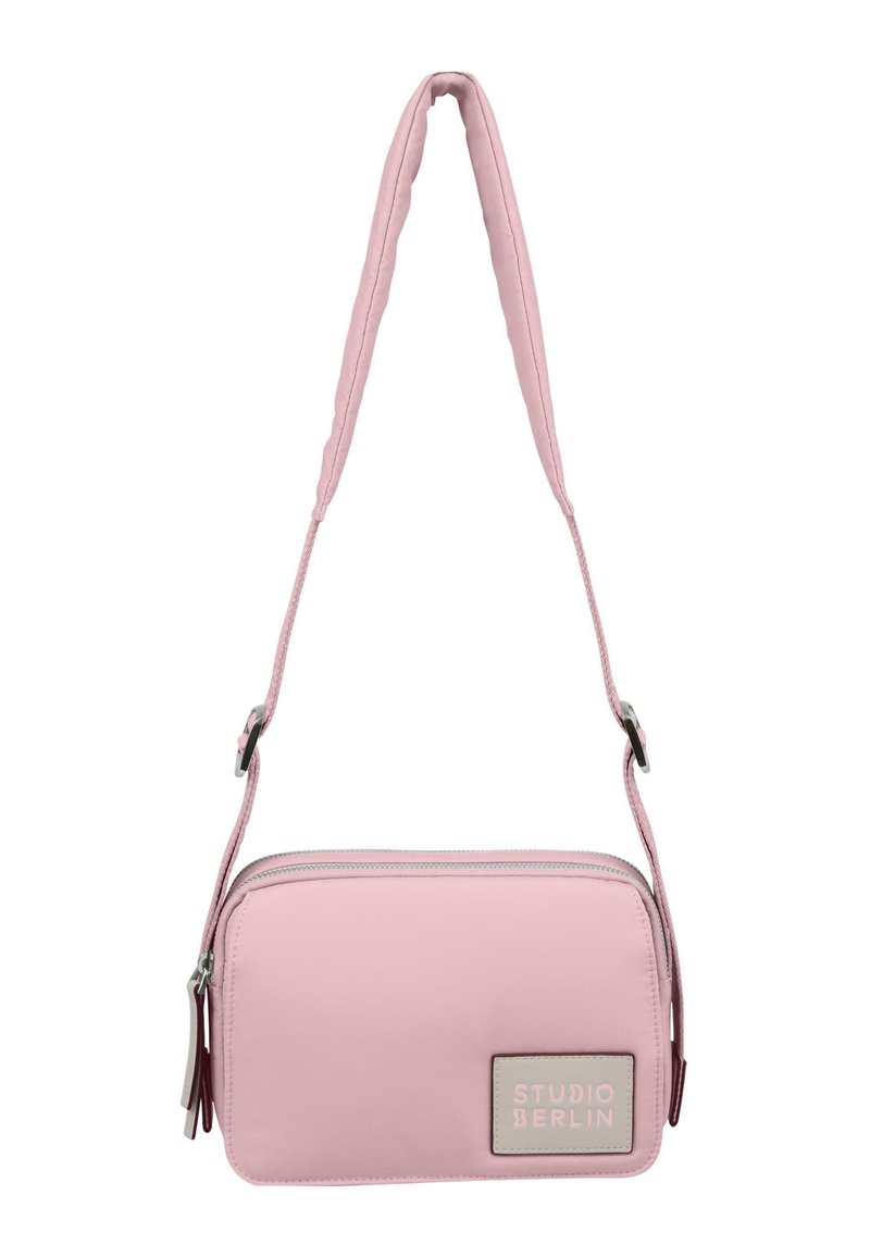 Borsa sintetica rosa con una sola tracolla regolabile, forma rettangolare, chiusura con zip e una toppa testurizzata con la scritta "STUDIO BERLIN."