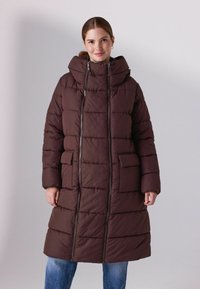 Pruun paksu jakk, millel on kõrge krae, tõmblukk ja ees taskud. Omab kokku õmmeldud tekstuuri ja puusani ulatuvat disaini.