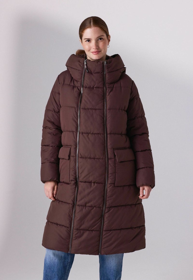 Pruun paksu jakk, millel on kõrge krae, tõmblukk ja ees taskud. Omab kokku õmmeldud tekstuuri ja puusani ulatuvat disaini.