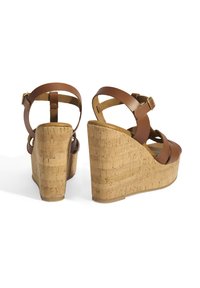 Sandales compensées en cuir marron avec une plateforme en liège, présentant des bandes entrecroisées et une sangle de cheville réglable avec des éléments en or.