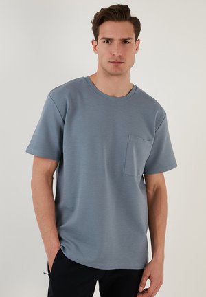 T-shirt a maniche corte con collo rotondo di colore azzurro, caratterizzato da un tessuto testurizzato e una tasca sul petto. Vestibilità liscia e rilassata.
