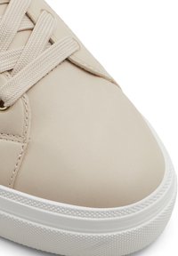 Beige syntetiska sneakers med en slät yta, framträdande snörningssystem, rund tå och vit gummisula med ett strukturerat greppmönster.