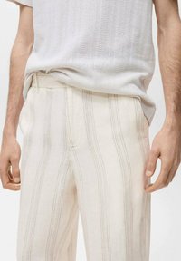 Pantalons en mélange de lin blanc cassé avec des rayures verticales gris clair. Présentent une coupe décontractée et un devant plat avec une ceinture.