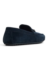 Mørkeblå ruskindsloafer med slip-on design, struktureret finish og gummisål. Har en stikning langs sømmen og en diskret metallisk detalje.