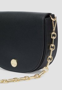 Schwarze Leder-Umhängetasche mit runder Form, goldener Kettenriemen und kreisförmigem Logo-Akzent auf der Vorderseite. Die strukturierte Oberfläche sorgt für Details.