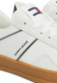 Sneakers bianchi con suola in gomma, parte superiore in pelle e camoscio, dettagli grigi e marchio "TOMMY JEANS" di lato e sulla linguetta.