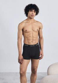 Boxeri din bumbac negri, cu un brâu imprimentat cu logo. Modelul are o constituție atletică, stând în fața unui fundal deschis.