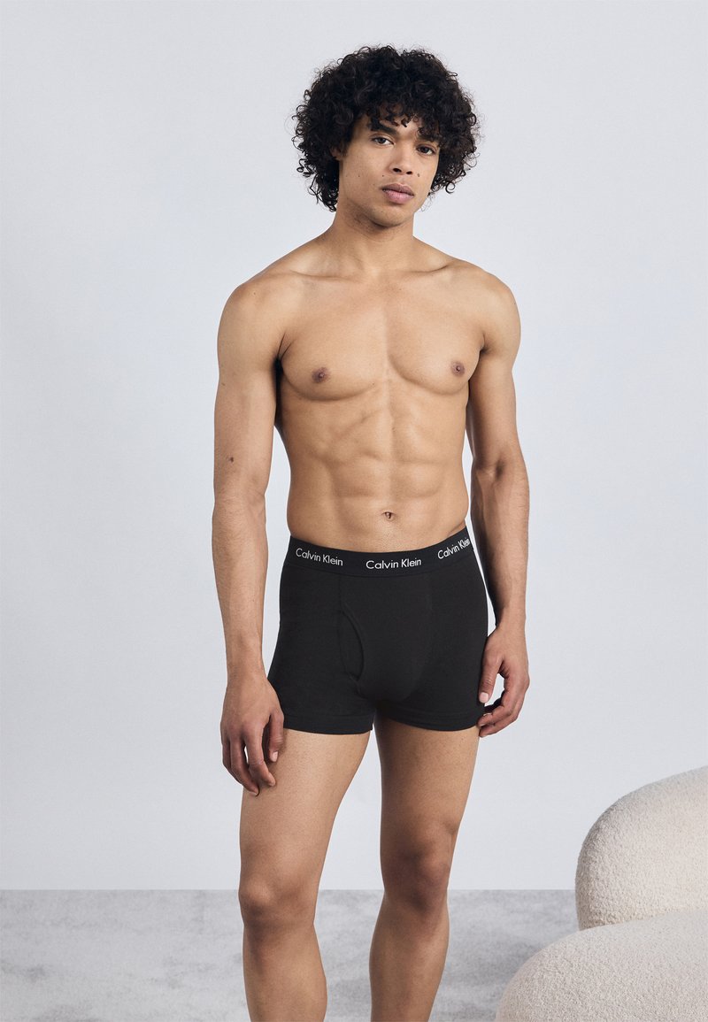 Boxeri din bumbac negri, cu un brâu imprimentat cu logo. Modelul are o constituție atletică, stând în fața unui fundal deschis.