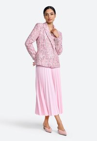 Blazer en tweed rose avec un design à double boutonnage, associé à une jupe midi plissée légère rose clair et des chaussures à talons pointus rose pâle.