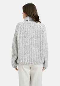 Grauer Strickpullover mit hohem Kragen und gerippter Textur, mit überschnittenen Schultern und lockerer Passform, kombiniert mit cremefarbener Hose.