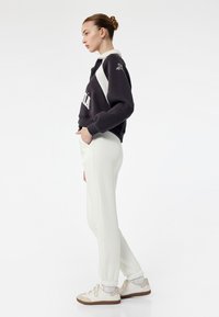 Elfenben joggers parret med en sort og hvid cropped sweatshirt med en lynlås krave og frontlogo. Modellen bærer hvide sneakers.