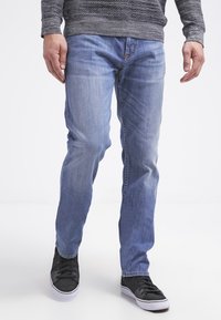 Jeans en denim bleu clair avec une coupe droite, présentant un léger délavage et un design classique à cinq poches, portés avec des baskets noires.